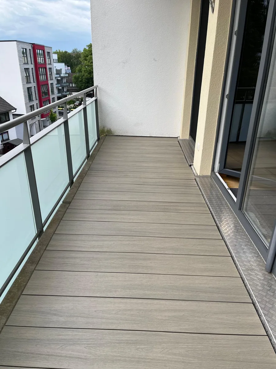 Neu sanierter Balkon mit grauem Dielenbelag und Glasbrüstung
