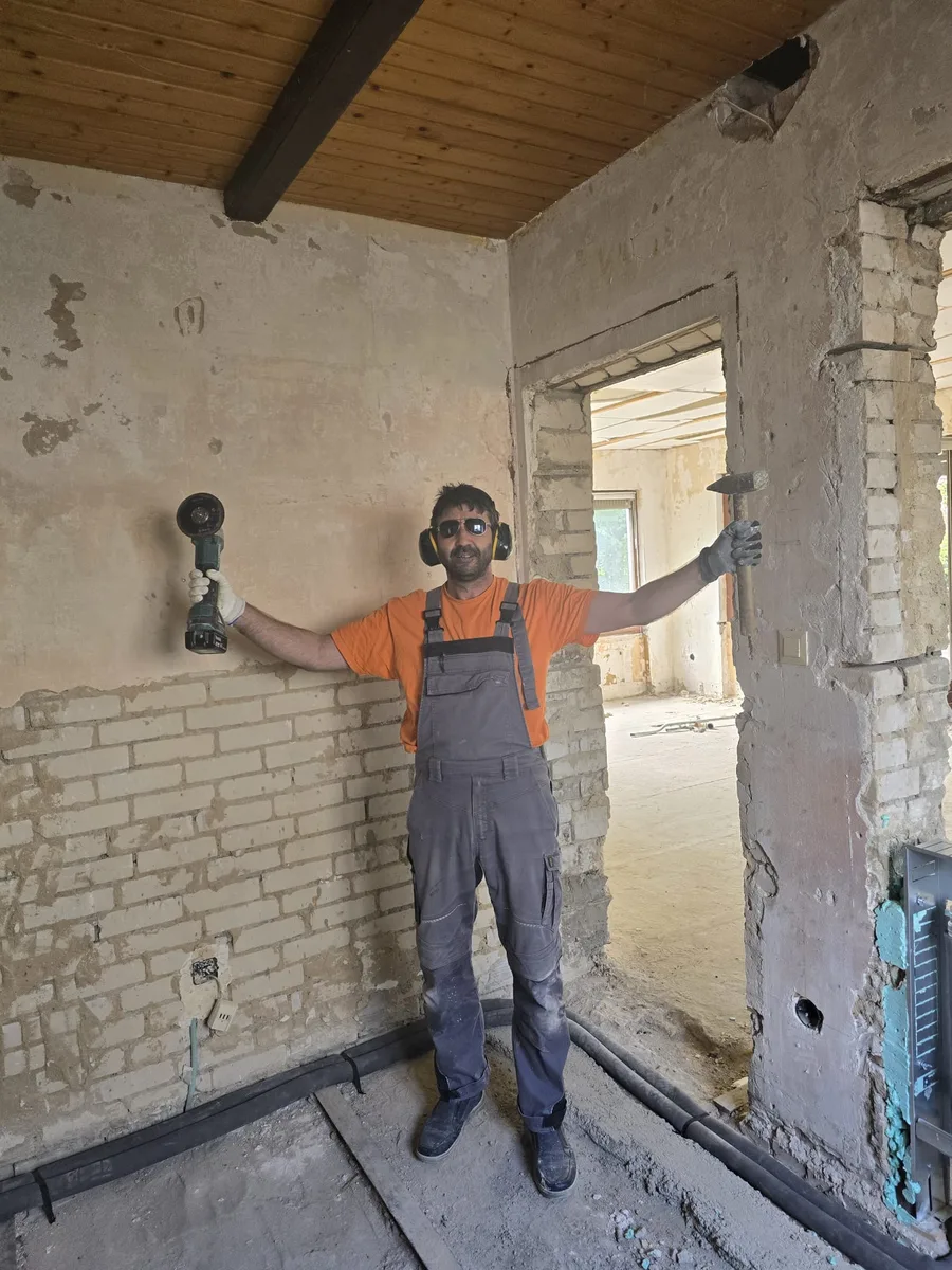 Handwerker steht mit Winkelschleifer neben einem frisch hergestellten Wanddurchbruch in einer Ziegelwand